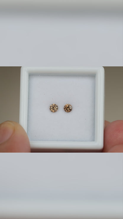 Video of the cognac brown diamond pair in a held white display box, with close face-up views and relative-scale context.