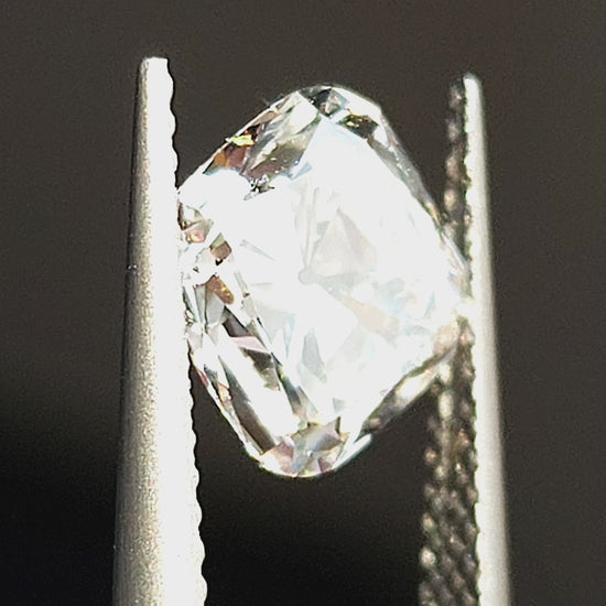 Square cushion Old Mine Cut diamond tilted in tweezers and displayed on fingertips, showing chunky facet reflections.