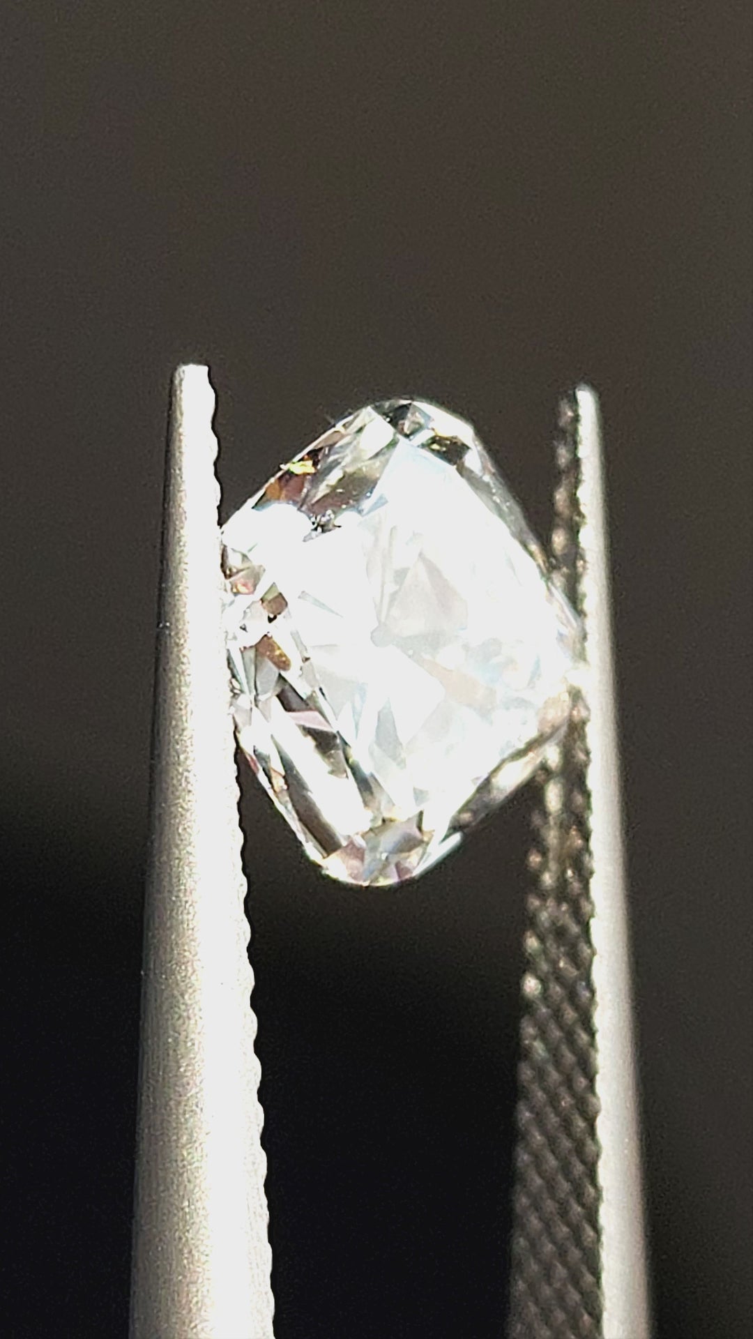 Square cushion Old Mine Cut diamond tilted in tweezers and displayed on fingertips, showing chunky facet reflections.