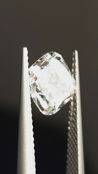 Square cushion Old Mine Cut diamond tilted in tweezers and displayed on fingertips, showing chunky facet reflections.