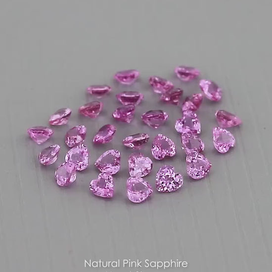 Representative parcel of pink heart-shaped sapphires viewed at changing angles on a gray surface; each purchase includes five selected sapphires.