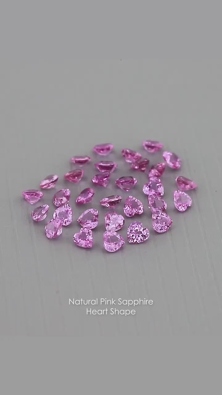 Representative parcel of pink heart-shaped sapphires viewed at changing angles on a gray surface; each purchase includes five selected sapphires.