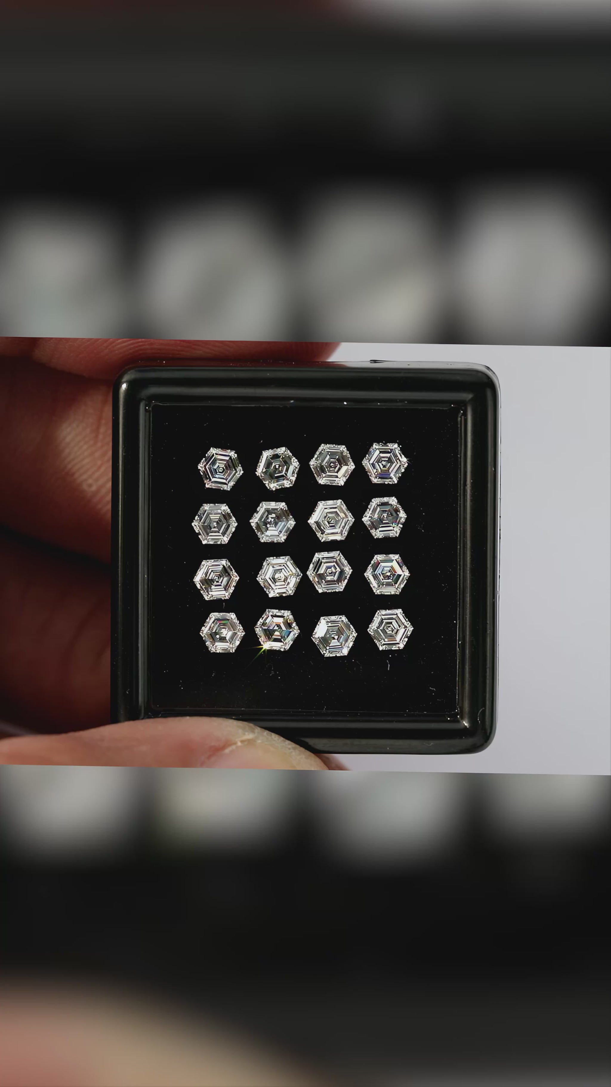 Video of hexagonal step-cut diamonds arranged face-up in a black tray held between fingers, with wider scale views and closer views of changing facet reflections.