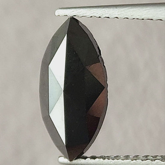Video of the black marquise rose-cut diamond face-up in tweezers, then on a fingertip and in a palm, showing its pointed outline and changing triangular facet reflections.