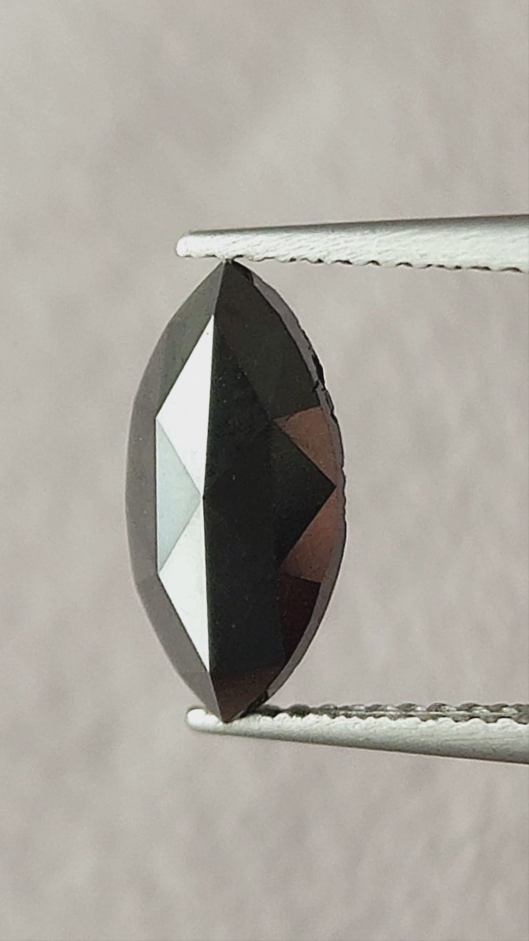 Video of the black marquise rose-cut diamond face-up in tweezers, then on a fingertip and in a palm, showing its pointed outline and changing triangular facet reflections.