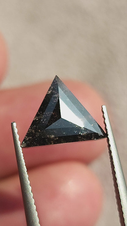 Triangular rose-cut salt and pepper diamond rotated in tweezers, showing crown, shallow profile and inclusions, followed by a view on fingertips for scale.