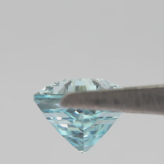 Aqua-blue hexagonal lab-grown sapphire turning in tweezers and shown between fingertips for scale.