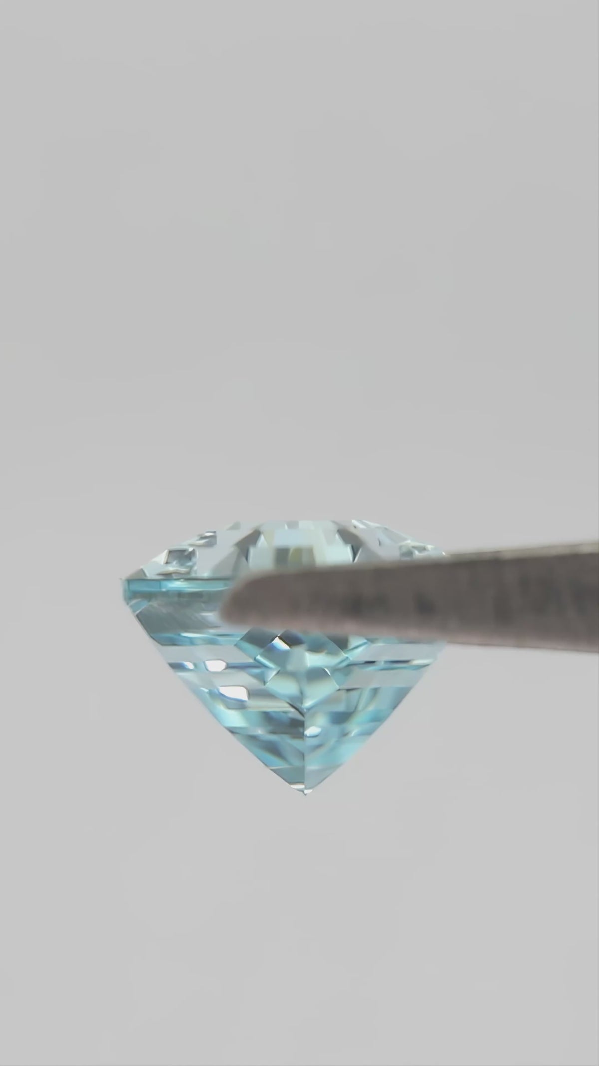 Aqua-blue hexagonal lab-grown sapphire turning in tweezers and shown between fingertips for scale.