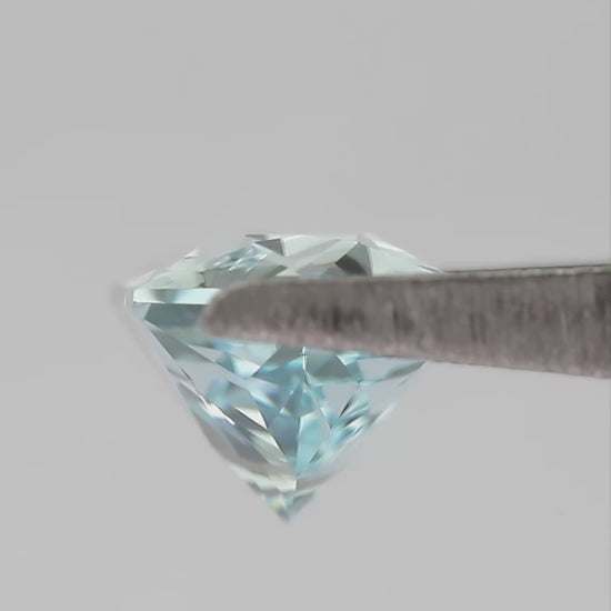 Aquamarine-blue lab-grown sapphire held in tweezers, showing its elongated hexagon cut as it turns.