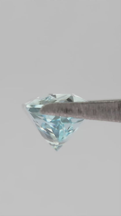 Aquamarine-blue lab-grown sapphire held in tweezers, showing its elongated hexagon cut as it turns.