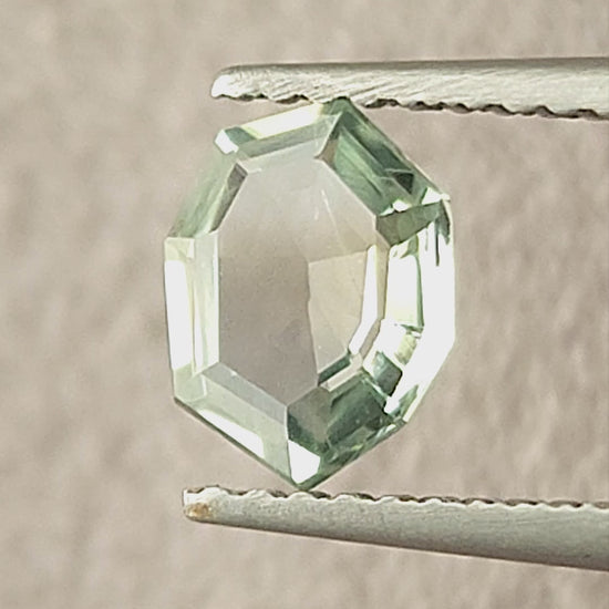 Mint green octagonal sapphire shown rotating in tweezers, between fingertips and on a white pad.