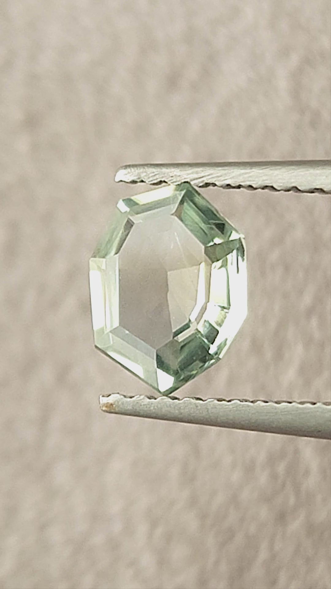 Mint green octagonal sapphire shown rotating in tweezers, between fingertips and on a white pad.