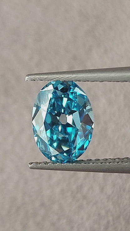 Blue oval diamond rotating in tweezers and then between fingertips, showing its broad facets and size.