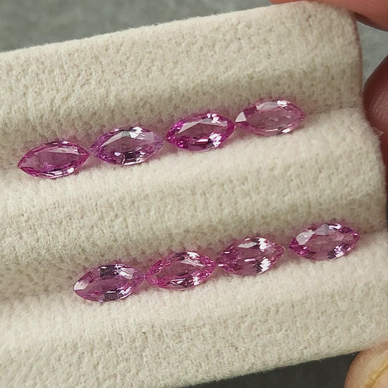 All eight pink marquise sapphires shown in rows on a grooved pad and grouped on a handheld white tray.