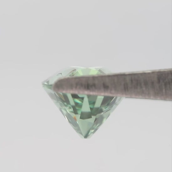 Mint-green lab-grown sapphire turning in tweezers and resting between fingertips for scale.
