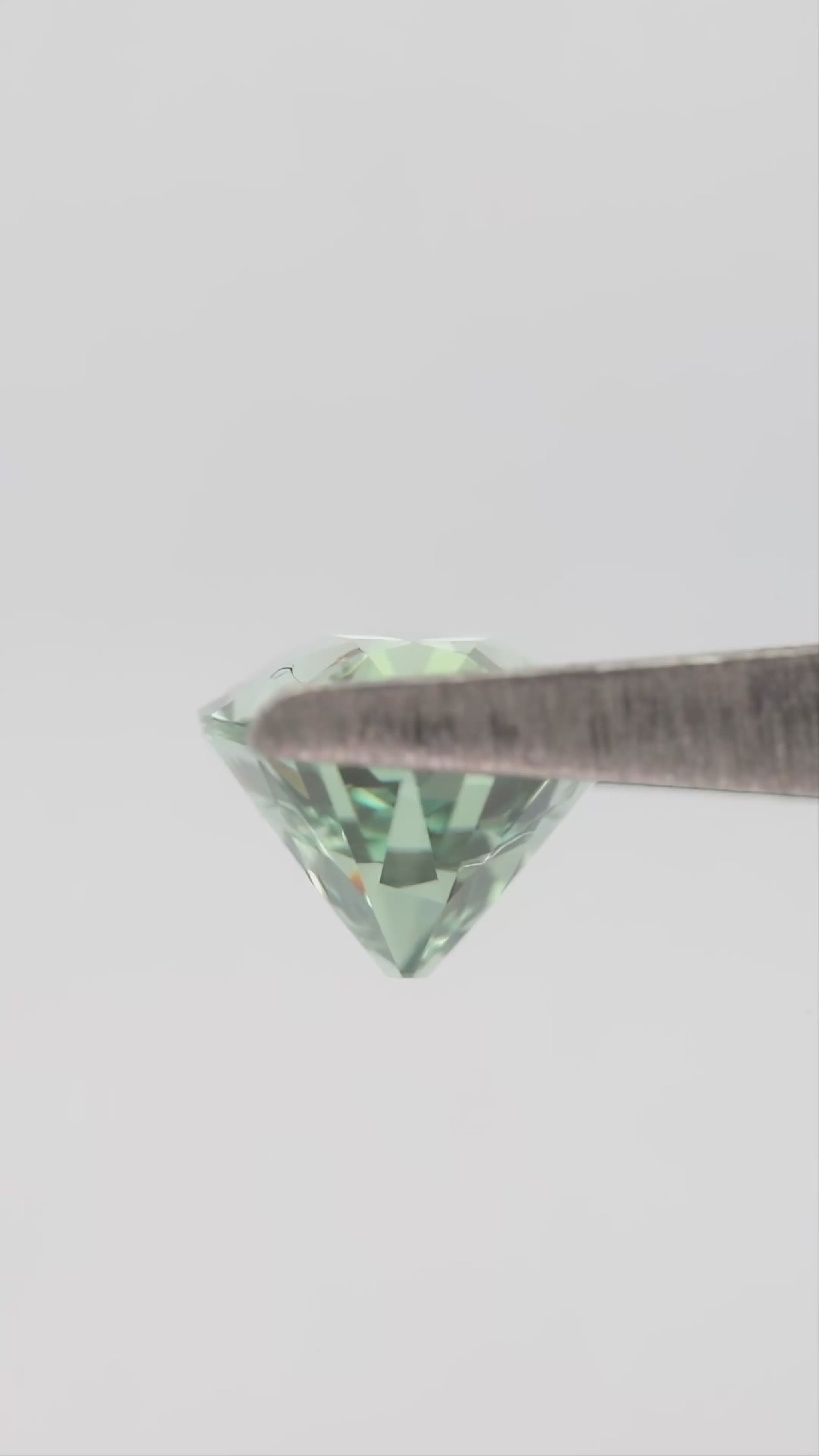 Mint-green lab-grown sapphire turning in tweezers and resting between fingertips for scale.