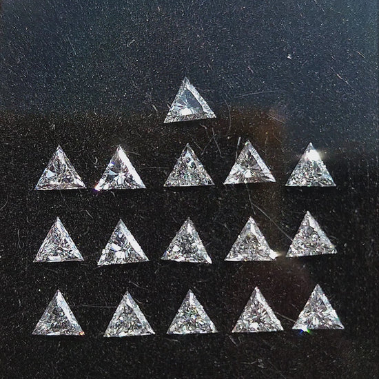 Calibrated triangle diamonds shown in a display box, as a single face-up stone in tweezers and loose in a palm; purchase unit remains one diamond.