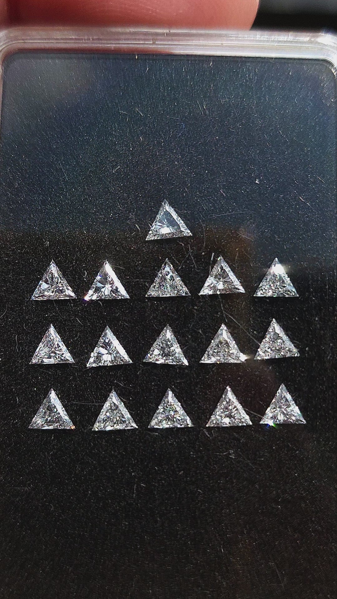 Calibrated triangle diamonds shown in a display box, as a single face-up stone in tweezers and loose in a palm; purchase unit remains one diamond.