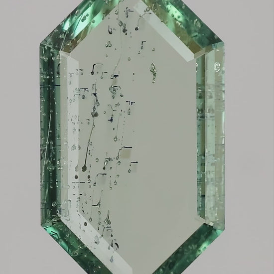 Video of the exact green lab-grown portrait-cut sapphire rotated in tweezers, showing its thin profile and scale on and between fingers.