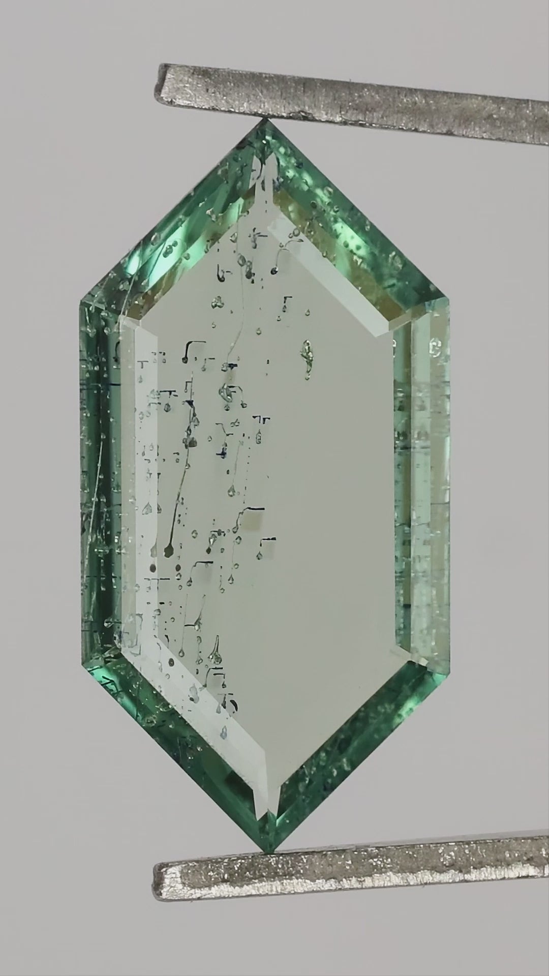 Video of the exact green lab-grown portrait-cut sapphire rotated in tweezers, showing its thin profile and scale on and between fingers.