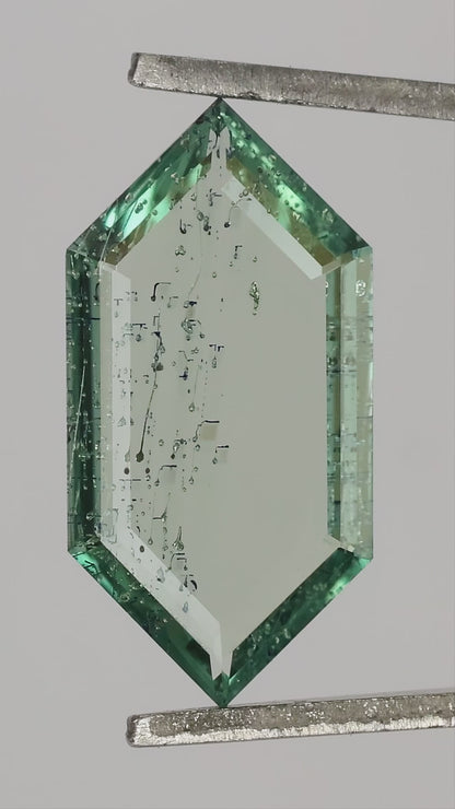 Video of the exact green lab-grown portrait-cut sapphire rotated in tweezers, showing its thin profile and scale on and between fingers.