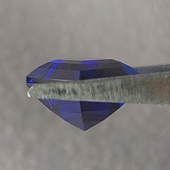 Royal blue lab-grown kite sapphire shown in tweezers from side and pavilion angles, followed by finger-held face-up scale views.