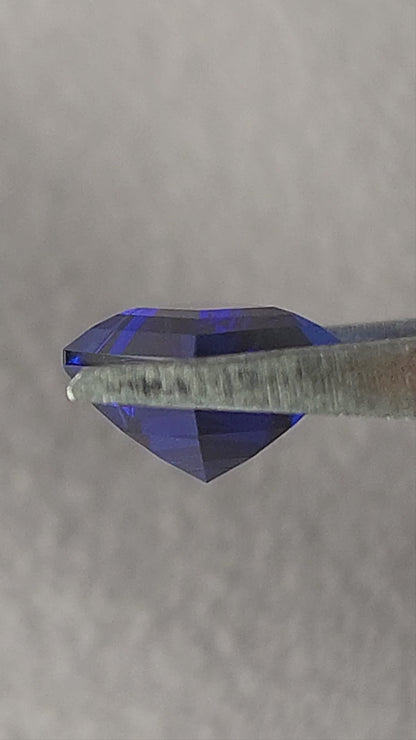 Royal blue lab-grown kite sapphire shown in tweezers from side and pavilion angles, followed by finger-held face-up scale views.