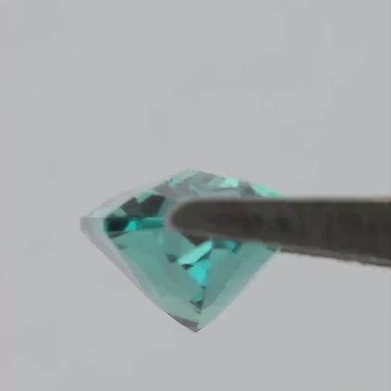 Reference 12 x 6 mm lab-grown alexandrite moving in tweezers, showing its elongated outline and shifting step-cut reflections.