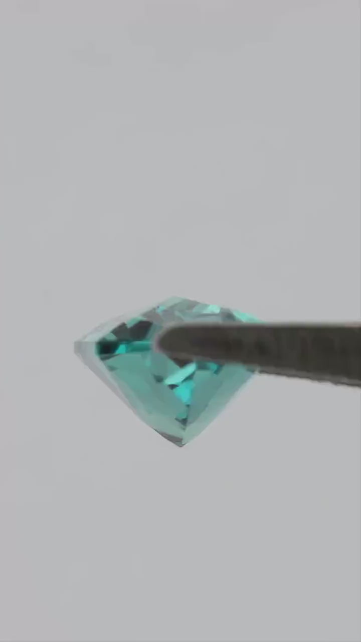 Reference 12 x 6 mm lab-grown alexandrite moving in tweezers, showing its elongated outline and shifting step-cut reflections.