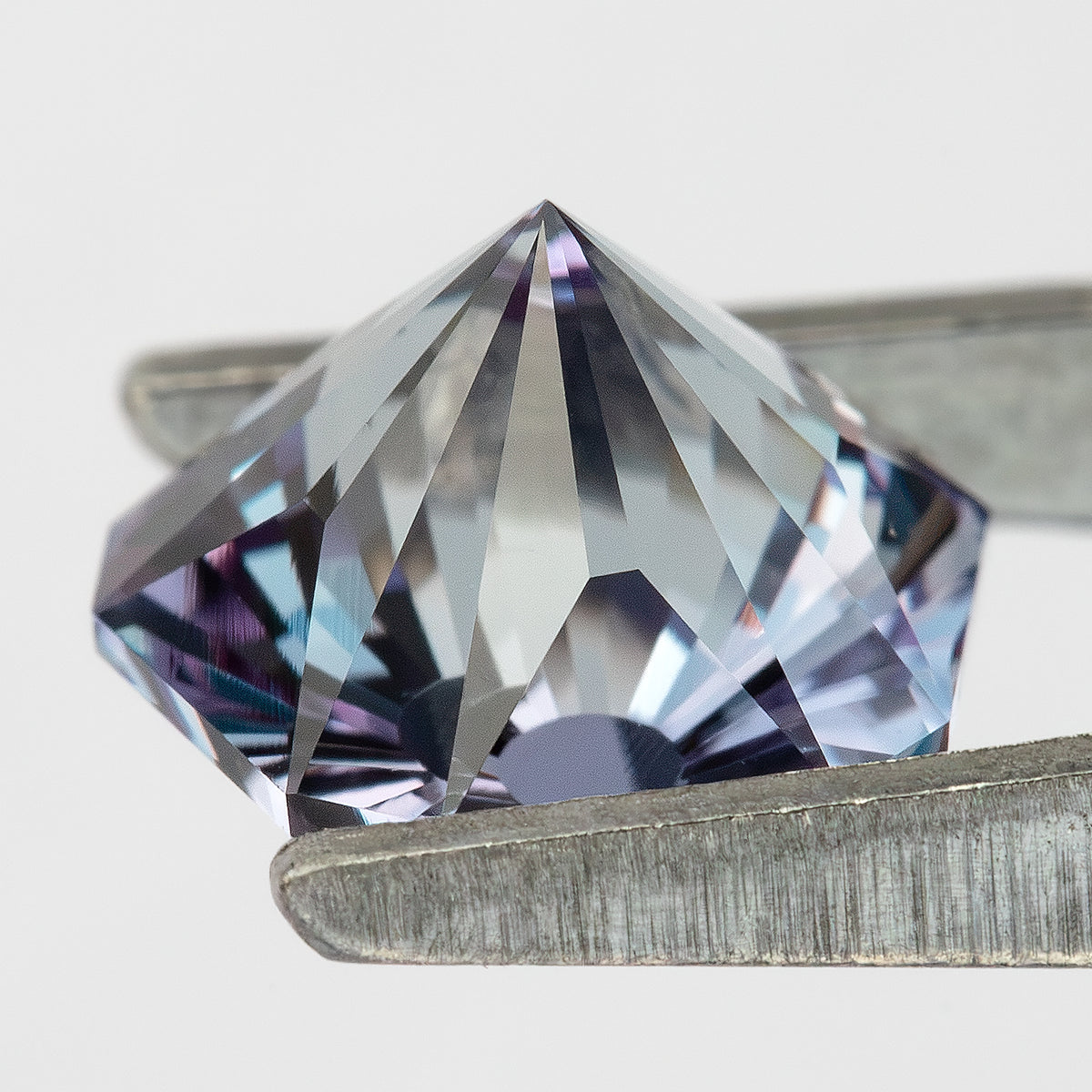 Oblique pavilion profile of the pentagon sapphire in tweezers, showing its pointed underside and depth.