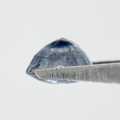 Side profile of the oval blue sapphire held in tweezers, showing crown and pavilion depth.