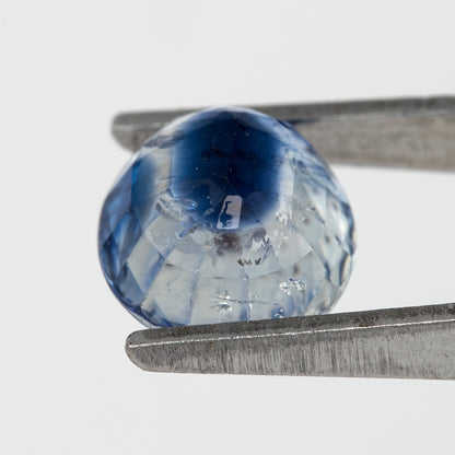 Tilted back view of the oval blue sapphire in tweezers, showing its pavilion facets.
