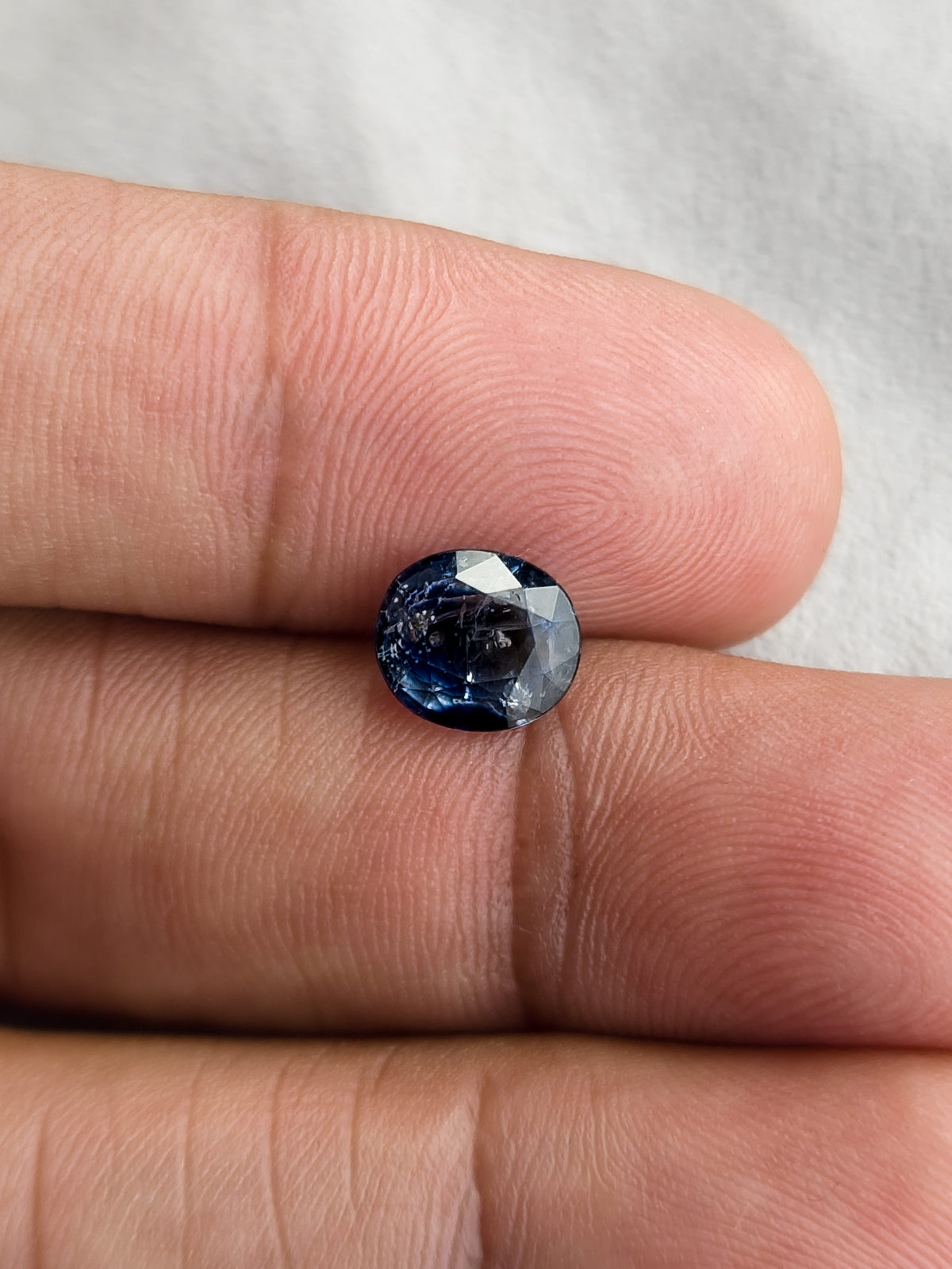 Face-up oval blue sapphire resting on fingers for a size reference.