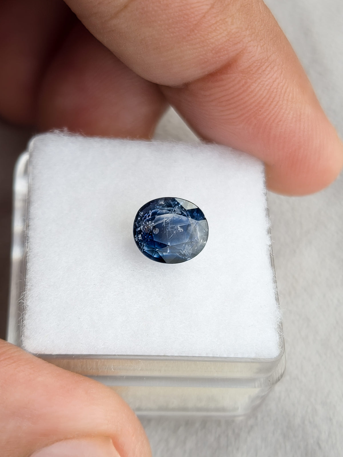 Face-up oval blue sapphire resting on a white display pad held in a hand.