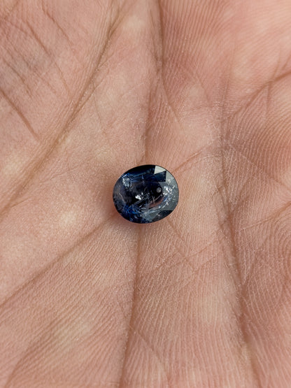 The loose oval blue sapphire resting face-up in a palm to show its scale.
