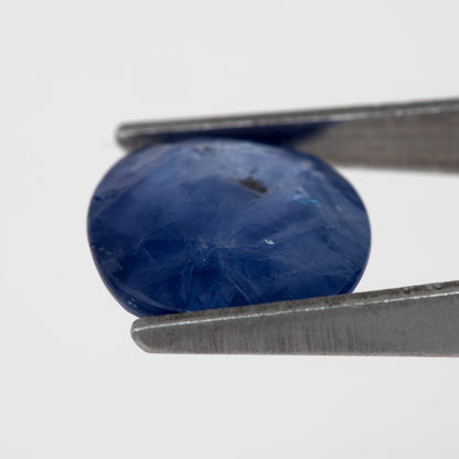 Tilted crown-side view of the oval blue sapphire in tweezers, showing a different pattern of facet reflections.
