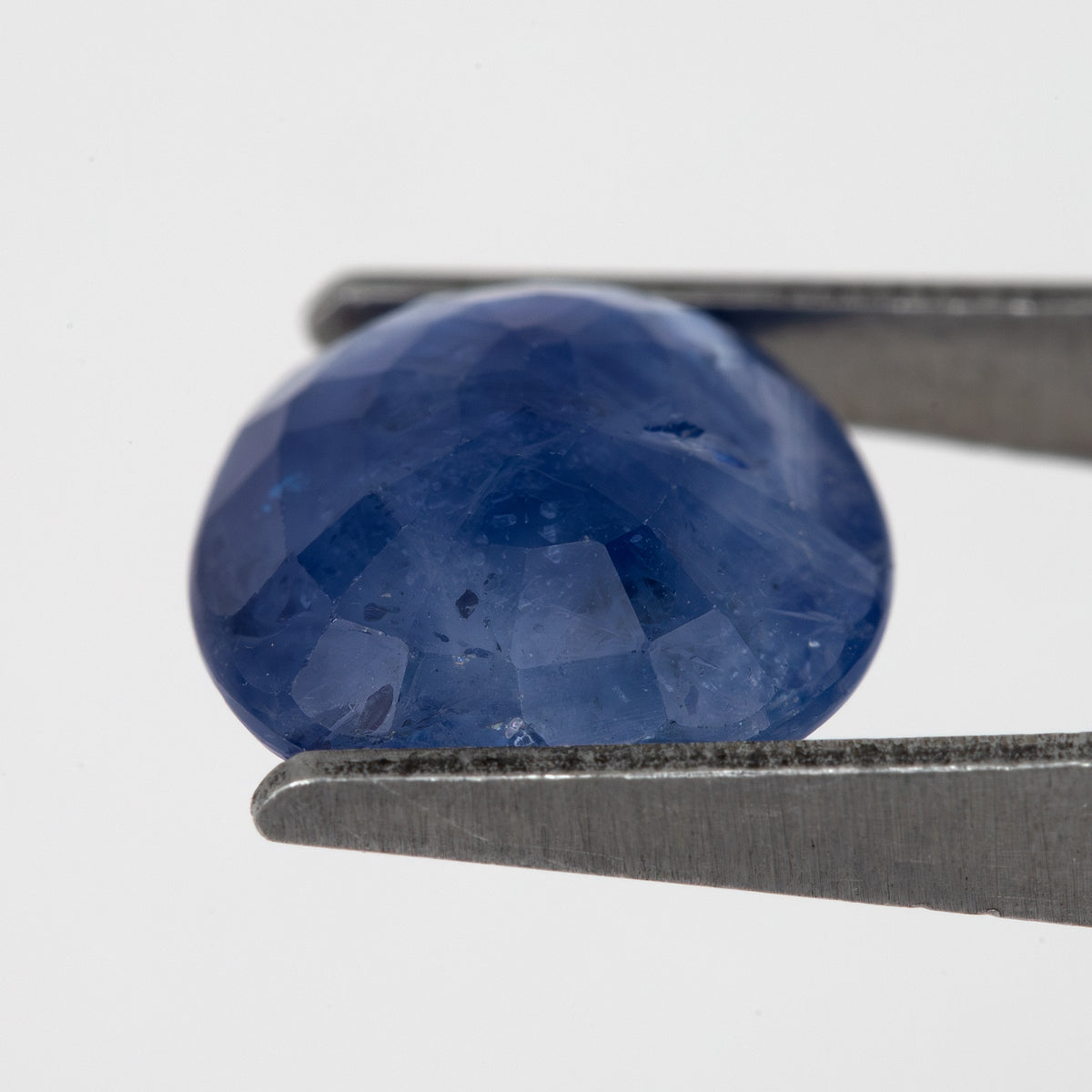 Tilted back view of the oval blue sapphire in tweezers, showing its pavilion facets.