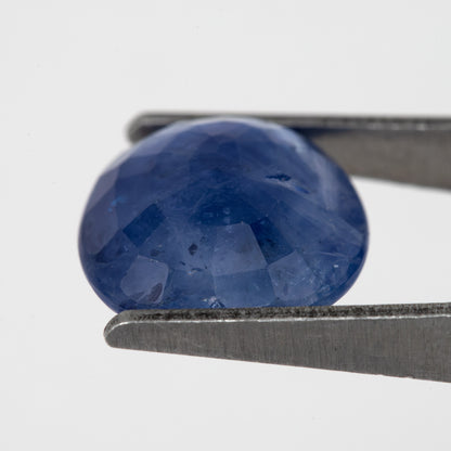 Tilted back view of the oval blue sapphire in tweezers, showing its pavilion facets.