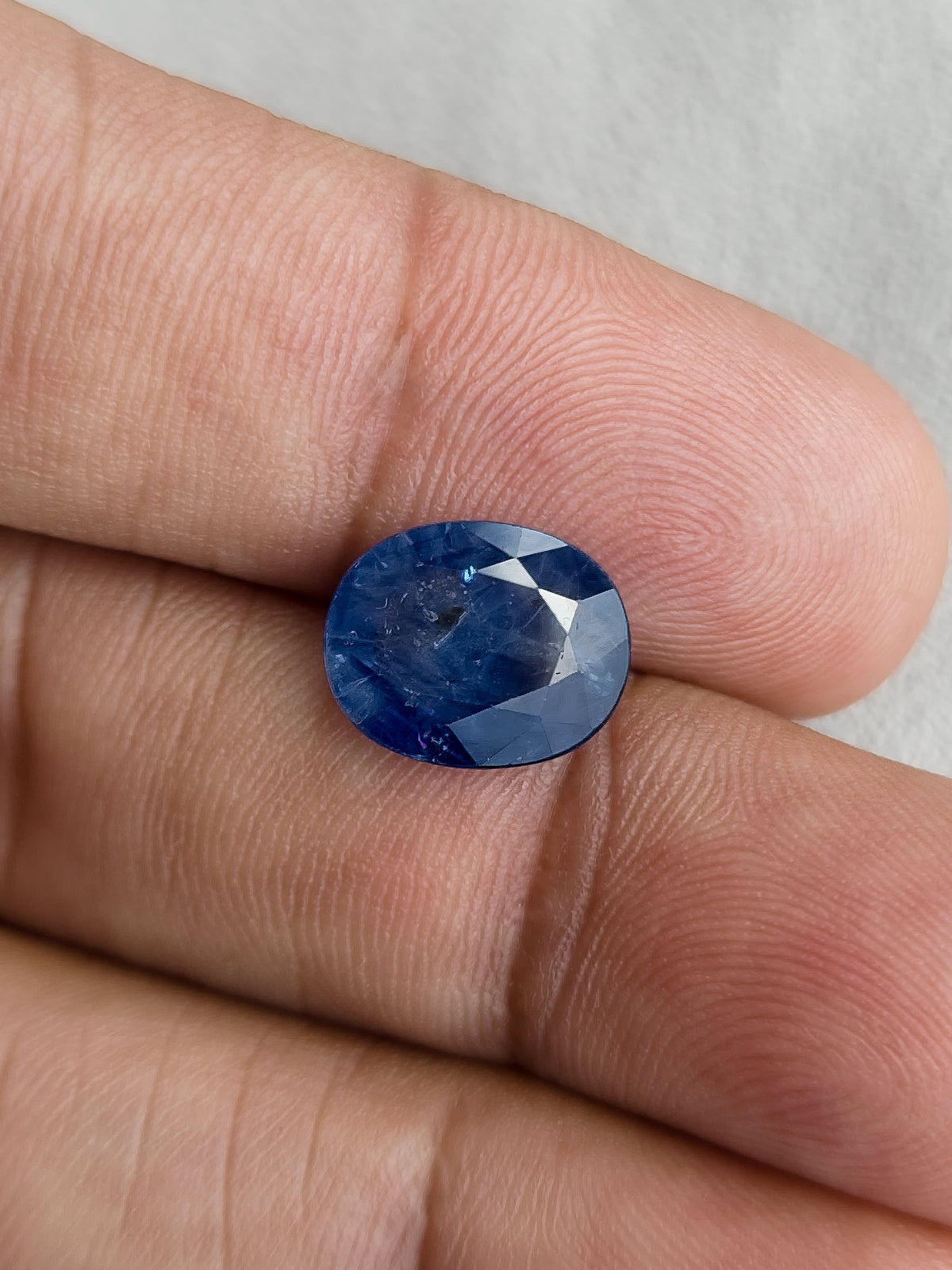 Face-up oval blue sapphire resting on fingers for a size reference.