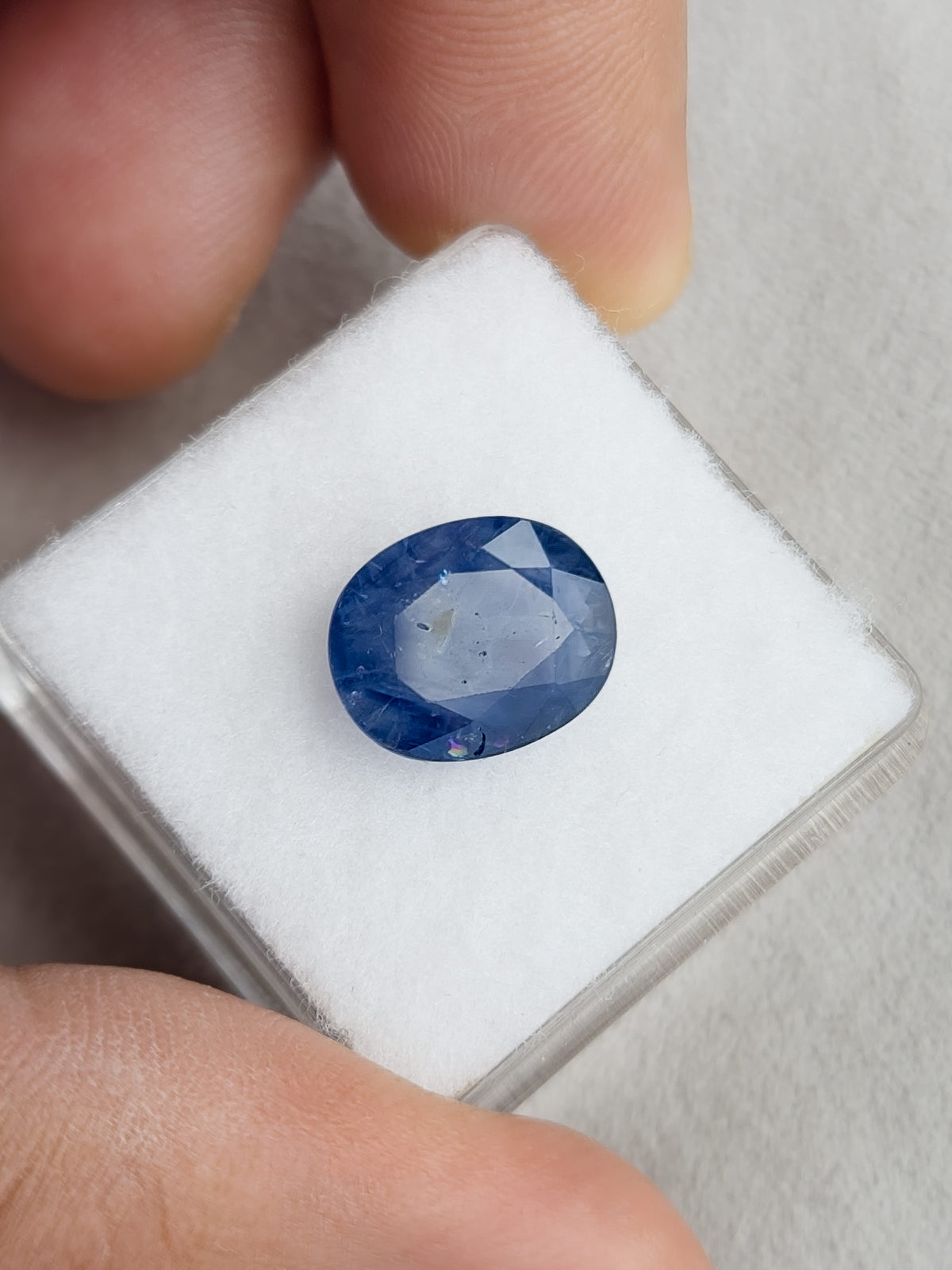 Face-up oval blue sapphire resting on a white display pad held in a hand.