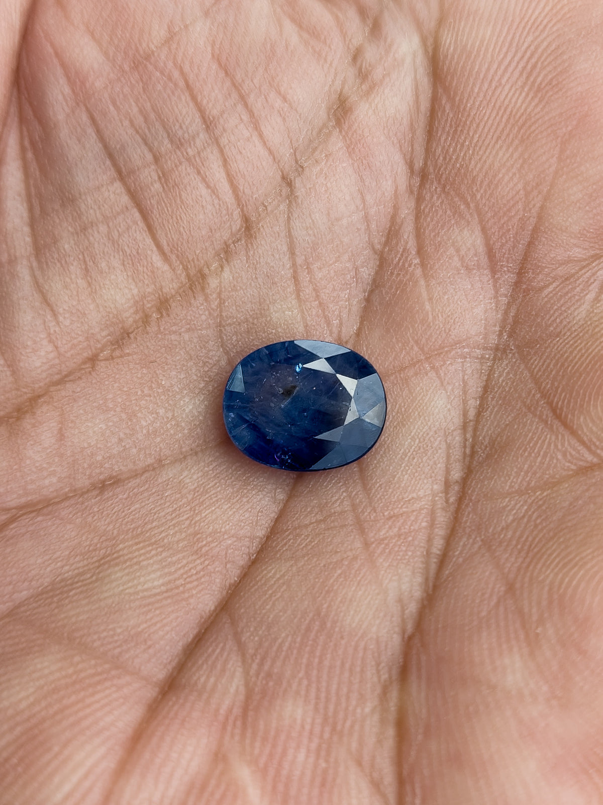 The loose oval blue sapphire resting face-up in a palm to show its scale.
