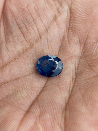 The loose oval blue sapphire resting face-up in a palm to show its scale.