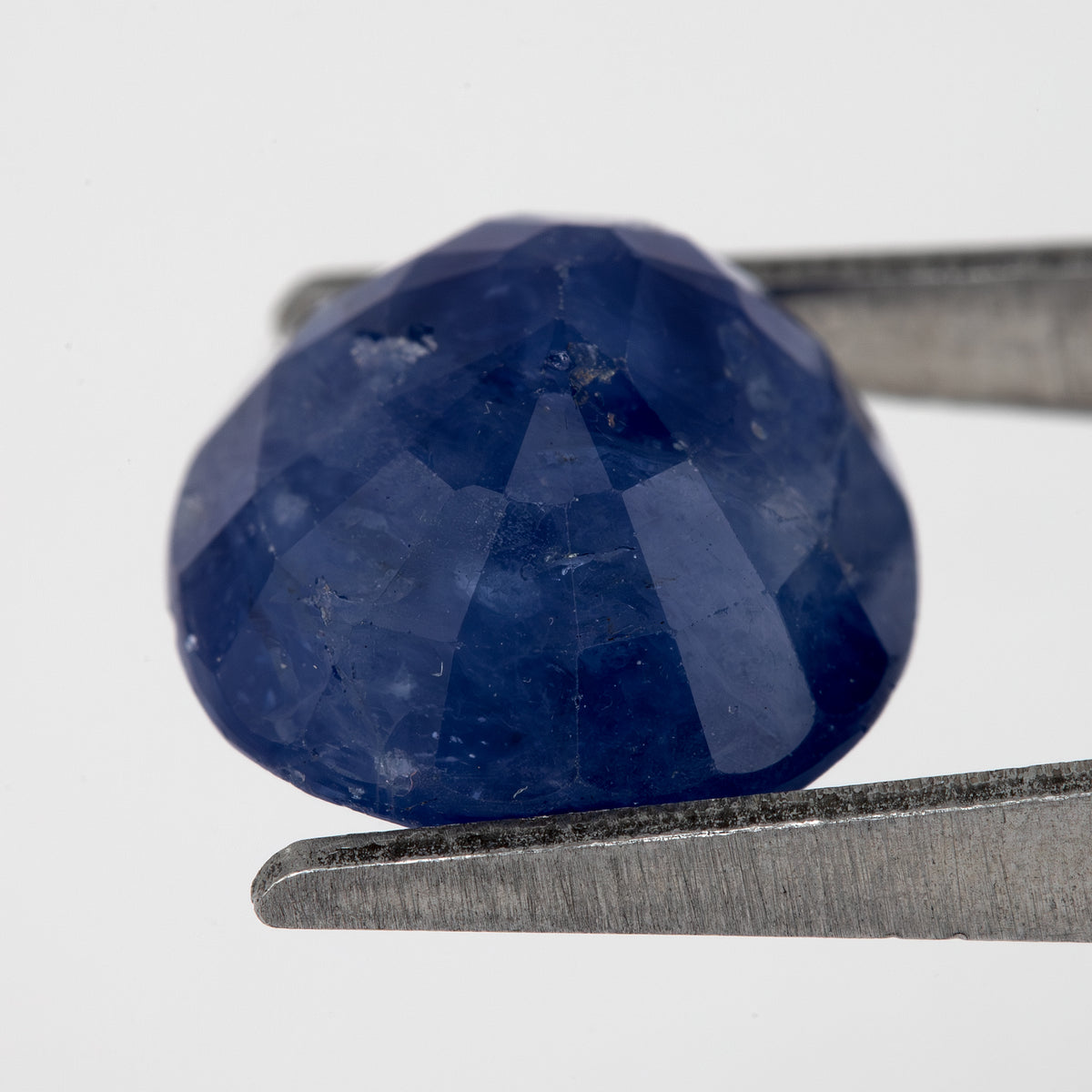 Tilted back view of the oval blue sapphire in tweezers, showing its pavilion facets.