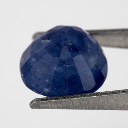 Tilted back view of the oval blue sapphire in tweezers, showing its pavilion facets.