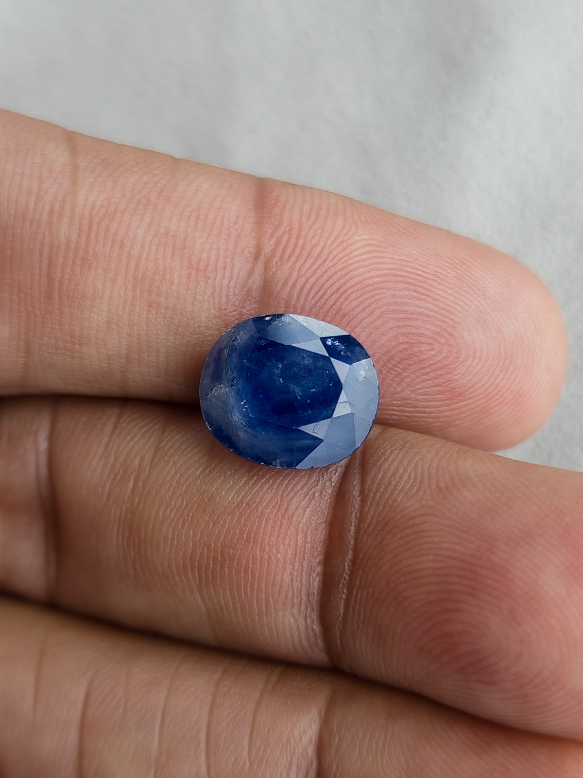 Face-up oval blue sapphire resting on fingers for a size reference.