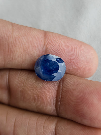 Face-up oval blue sapphire resting on fingers for a size reference.