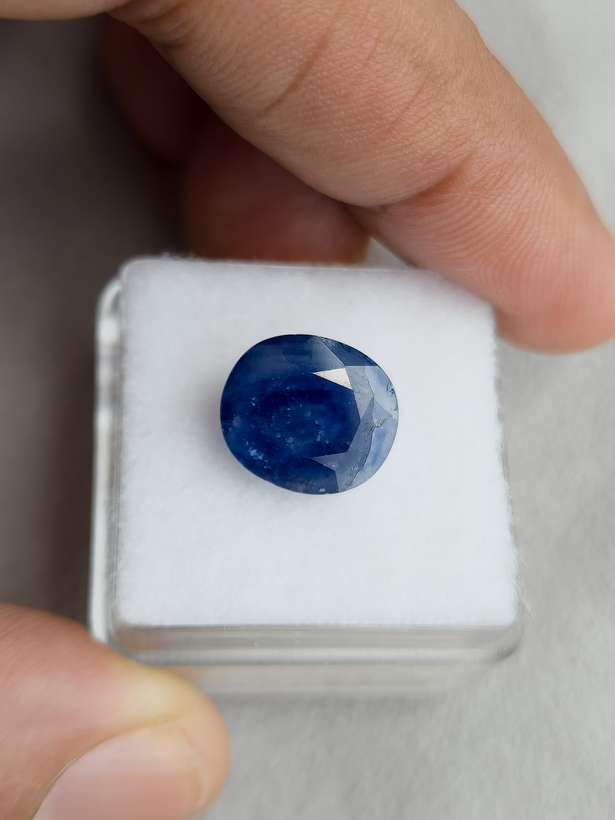 Face-up oval blue sapphire resting on a white display pad held in a hand.
