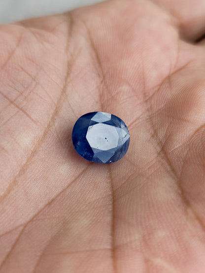 The loose oval blue sapphire resting face-up in a palm to show its scale.