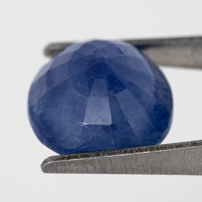 Tilted back view of the oval blue sapphire in tweezers, showing its pavilion facets.