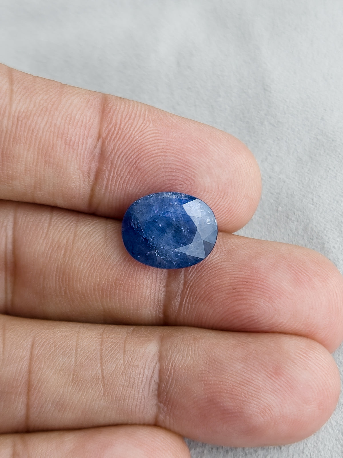 Face-up oval blue sapphire resting on fingers for a size reference.